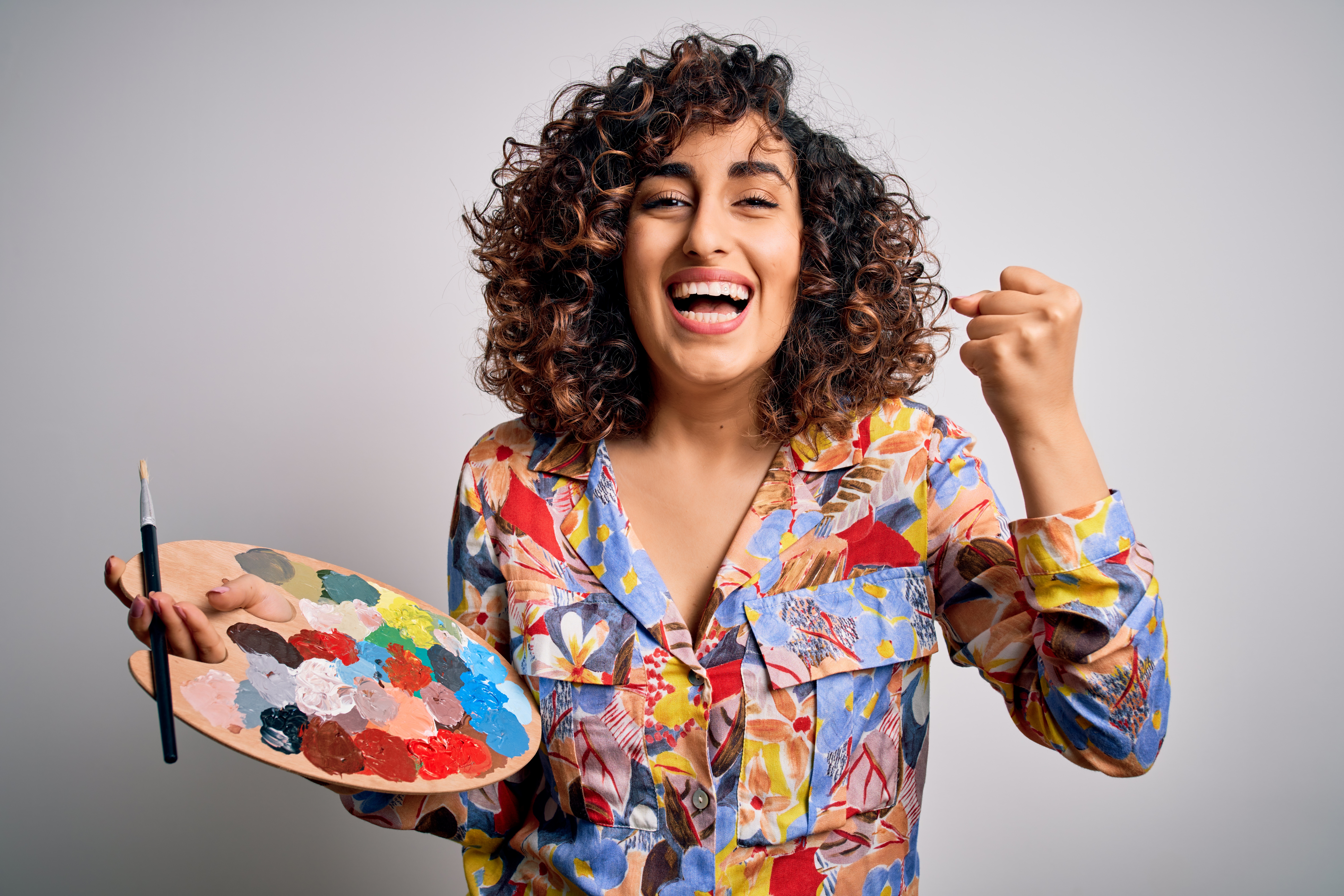 Young beautiful curly arab artist woman painting using brush and palette with colors screaming proud and celebrating victory and success very excited, cheering emotion